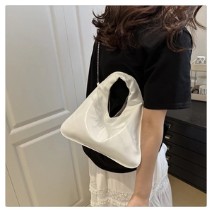 Close-up of white patent leather hobo bag featuring a silver chain strap on model