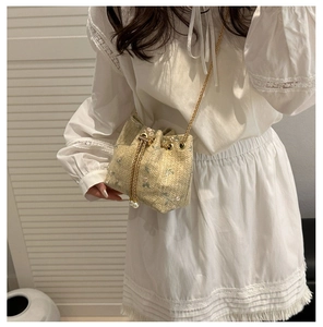 Detail of straw bucket bag with floral embroidery, gold chain, and pearl drawstrings