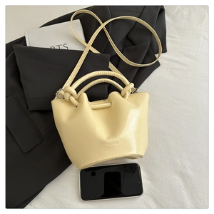 Pale yellow leather bucket bag size comparison with a smartphone on white fabric