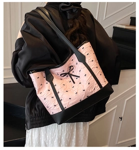 Close-up of pink tote bag featuring black bow patterns and elegant leather shoulder strap