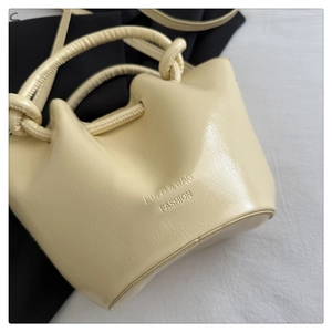 Detailed macro view of the twisted handle design and luxury embossed logo on cream bucket bag