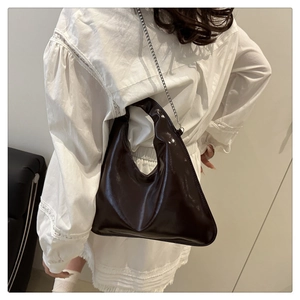 Close-up of asymmetric dark brown patent leather bag with silver chain strap on a model