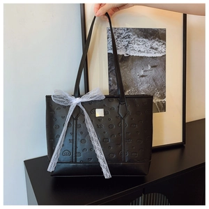 Close-up of black embossed tote bag with lace bow detail and silver logo plaque