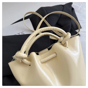 Detail of beige pleated bucket bag featuring knotted handles and glossy synthetic leather