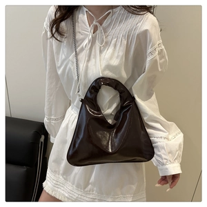 Detail of dark brown glossy handbag with round handle and silver chain shoulder strap