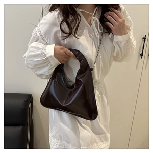 Detailed view of dark brown glossy handbag with silver chain strap and top handle