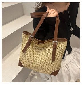 Straw tote bag with brown leather handles and silver buckles shown on a model