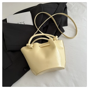 Détail du sac seau en PU beige brillant avec poignées nouées et bandoulière fine