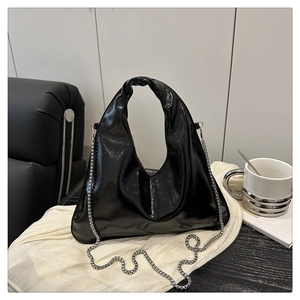 Detail of glossy black faux leather tote featuring silver chain strap and knotted handle