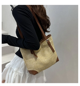 Side view of large straw tote bag with brown leather trim worn by model on stairs