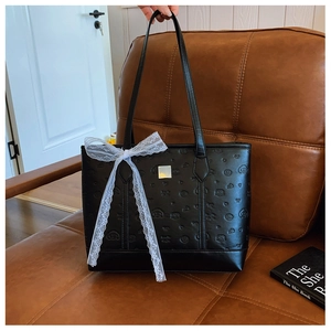 Detail of black embossed tote bag with silver plaque and white lace bow on sofa