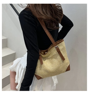 Detail of hand-woven straw tote bag with brown leather trim and metal buckles