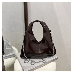 Detail of dark brown glossy handbag with circular handle and silver chain strap on art stool