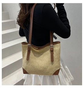 Close-up of woven straw tote bag featuring brown leather trim and metal buckle detail