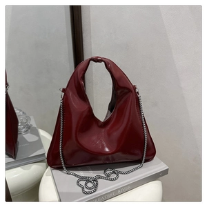 Detail of dark red glossy patent leather handbag with delicate metal chain strap