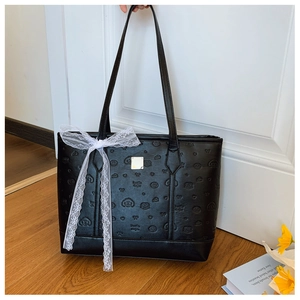 Detail of black leather tote bag with embossed pattern, metal hardware, and lace bow