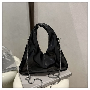 Detail of black glossy handbag with knot handle and silver chain strap on white stool
