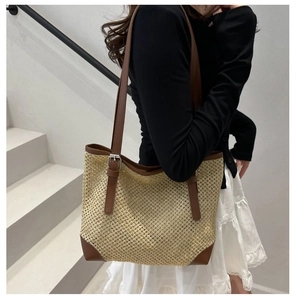 Detail of hand-woven straw tote with brown leather straps and reinforced corners