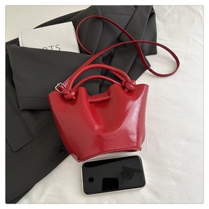 Top view of red patent leather bucket bag with phone for scale on white fabric