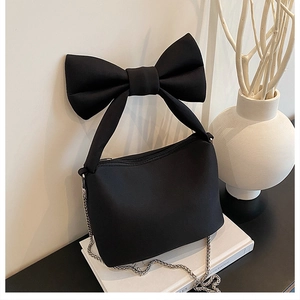 Close-up of stylish black canvas handbag featuring a large decorative 3D bow and silver chain