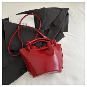 Close-up of bright red pleated bucket bag with knotted handle and shiny patent finish