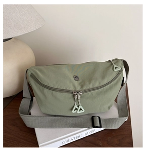 Detail of avocado green nylon chest bag with adjustable grey strap on a book base