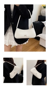 Close-up of white leather baguette bag featuring a decorative metallic bow detail