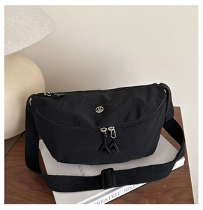 Close-up of black nylon crescent bag with metal 'M' logo on a wooden desk setting
