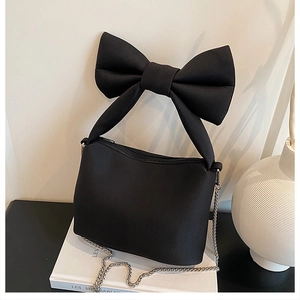 Close-up of black canvas bow handbag with silver chain on minimalist white props