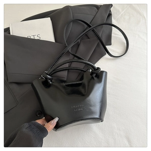 Detail of black pleated bucket bag with glossy finish and logo embossing on leather