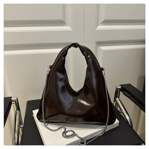 Detail of dark brown patent leather hobo bag with a silver bead chain and knotted handle