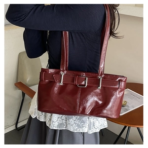 Detail of burgundy glossy faux leather underarm bag with silver buckle worn by a model