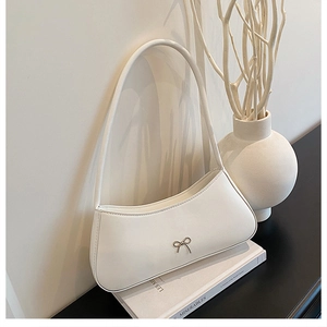 Detail of white faux leather baguette bag featuring a metallic bow and sleek curved structure