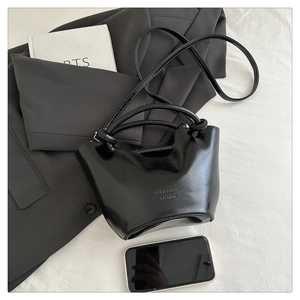 Detail of black glossy leather bucket bag with embossed logo and elegant top handle