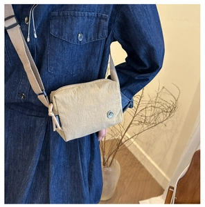 Detailed macro view of the beige nylon crossbody bag with metallic logo and side label