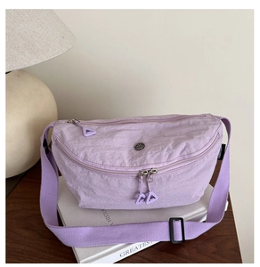 Detail of purple nylon crossbody bag with three zippers and metal logo on a book