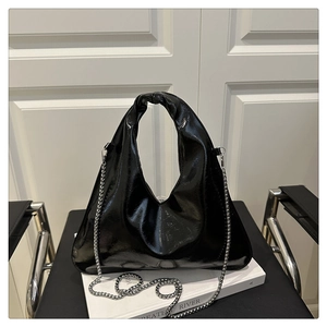 Detail of black glossy triangular handbag with elegant knotted handle and silver chain