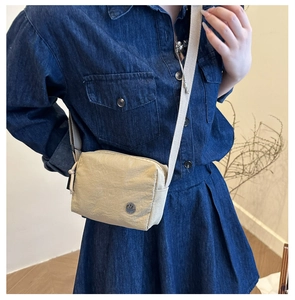 Detail of a beige nylon crossbody bag with metal M logo on a model in denim