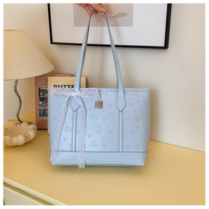 Detail of light blue embossed tote bag featuring a large white lace bow and shoulder straps
