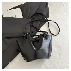 Detail of glossy black pleated bucket bag with a shiny leather texture and drawstring design
