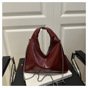Detail of burgundy glossy triangular handbag with silver chain on white books