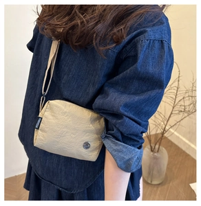 Detail of beige pleated crossbody bag with FANYISSA label and silver M metal badge