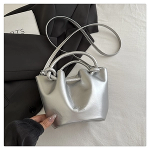 Detail of silver pleated bucket bag featuring knotted handles and metallic finish