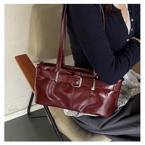 Detail of burgundy patent leather underarm bag with decorative belt buckle and shoulder straps