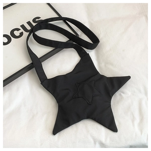 Flat lay of star-shaped black canvas crossbody bag with broad strap on white fabric