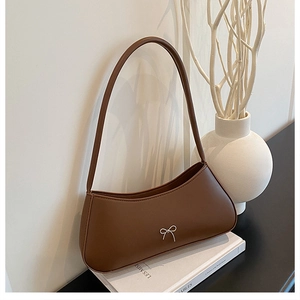 Detail of a brown leather shoulder bag with a silver metal bow accent on white books