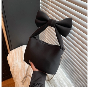 Detail of black bow-knot handbag featuring a fabric texture and metallic chain strap