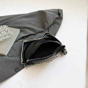 Chic black crescent moon bag with wide contrast strap and silver chain on a grey blazer