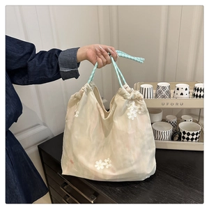 Detail of floral embroidery on beige tote bag with blue and white gingham handles