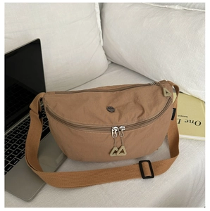 Detail of khaki nylon crescent bag with dual zippers and laptop on white bedding